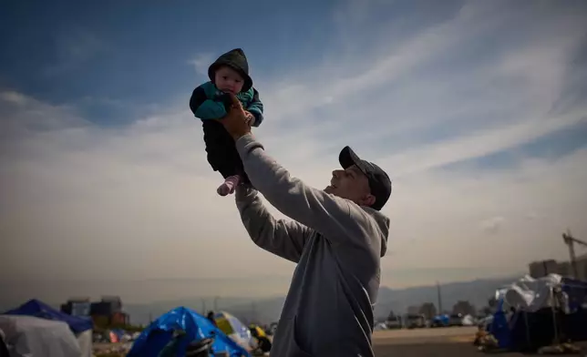 Abed Driss, displaced with his family from Beirut's southern suburbs of Dahiyeh, holds up his son Benin, 3 months, next to a tent used as a shelter in Beirut, Lebanon, Saturday, March 28, 2026. (AP Photo/Emilio Morenatti)