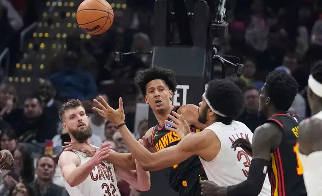 Cleveland Cavaliers center Jarrett Allen, right, reaches for the ball with teammate Dean Wade (32) and Atlanta Hawks forward Jalen Johnson, center, in the first half of an NBA basketball game in Cleveland, Wednesday, April 8, 2026. (AP Photo/Sue Ogrocki)