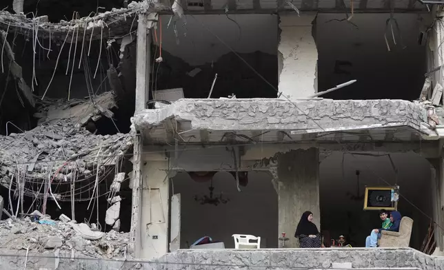 The wife and children of Fadi Al Zein, who lost both his homes in Israeli strikes in his village of Khiam and in Dahiyeh, sit on the balcony of their heavily damaged apartment building in Beirut's southern suburbs, Lebanon, Saturday, April 25, 2026. (AP Photo/Hassan Ammar)
