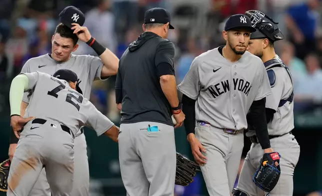 New York Yankees starting pitcher Elmer Rodriguez, right front, walks to the dugout after turning the ball over to manager Aaron Boone, center left, as José Caballero (72), Ben Rice, left rear, and J.C. Escarra, right rear, stand on the mound in the fifth inning of a baseball game against the Texas Rangers Wednesday, April 29, 2026, in Arlington, Texas. (AP Photo/Tony Gutierrez)