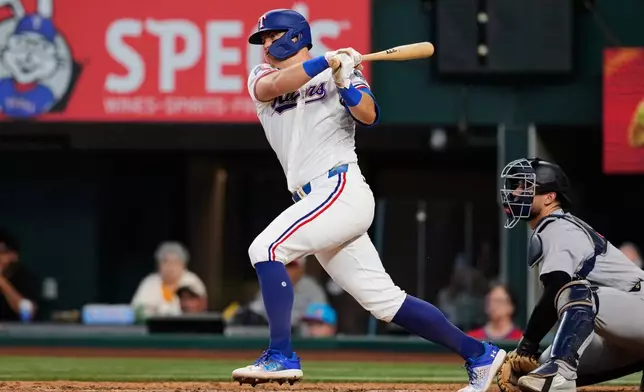 Texas Rangers' Josh Jung follows through on a two-run single as New York Yankees catcher J.C. Escarra, right, looks on in the fifth inning of a baseball game Wednesday, April 29, 2026, in Arlington, Texas. (AP Photo/Tony Gutierrez)