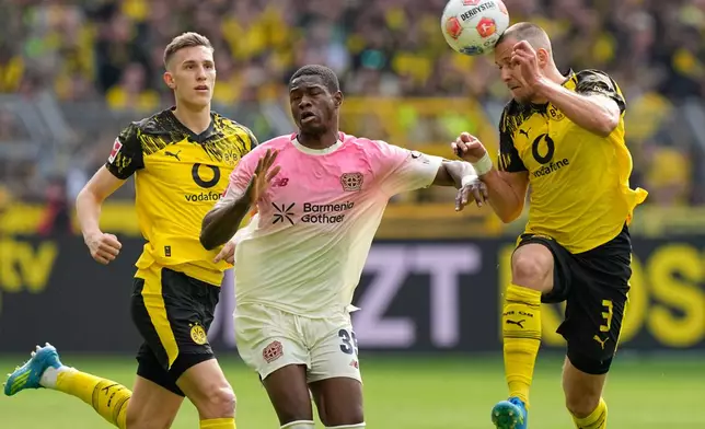 Dortmund's Waldemar Anton, right, challenges for the ball with Leverkusen's Christian Kofane, center, during the German Bundesliga soccer match between Borussia Dortmund and Bayer Leverkusen in Dortmund, Germany, Saturday, April 11, 2026. (AP Photo/Martin Meissner)