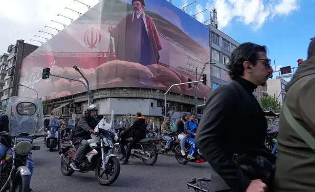 People drive their motorbikes past a billboard that shows a graphic depicting Iran's Supreme Leader Ayatollah Mojtaba Khamenei in downtown Tehran, Iran, Monday, April 6, 2026. (AP Photo/Vahid Salemi)