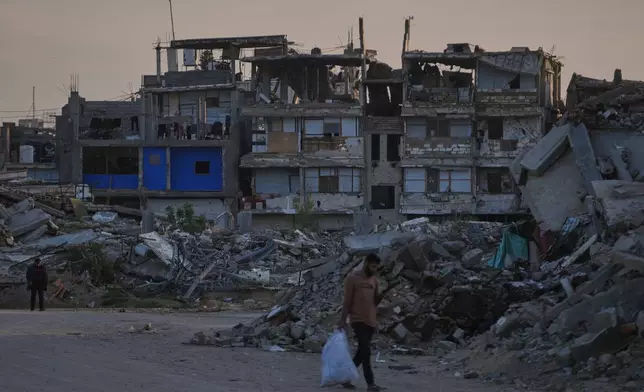 Palestinians walk along a street surrounded by buildings destroyed during Israeli air and ground operations in Khan Younis, southern Gaza Strip, Thursday, April 9, 2026. (AP Photo/Abdel Kareem Hana)