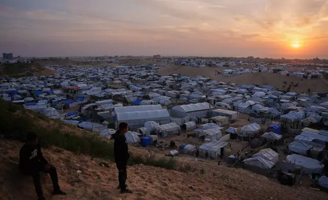 Palestinians youth look on as they stand in an area next to tents at a makeshift camp for displaced people, at sunset in Khan Younis, southern Gaza Strip, Thursday, April 9, 2026. (AP Photo/Abdel Kareem Hana)