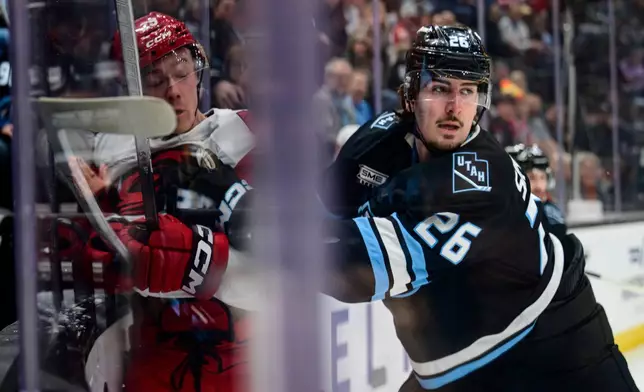 Utah Mammoth defenseman Dmitri Simashev (26) checks Carolina Hurricanes left wing Bradly Nadeau, left, into the boards during the first period of an NHL hockey game, Saturday, April 11, 2026, in Salt Lake City. (AP Photo/Tyler Tate)
