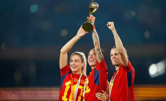FILE - Spain's Alexia Putellas, Jennifer Hermoso and Irene Paredes ,from left, celebrate with the trophy at the end of the Women's World Cup soccer final between Spain and England at Stadium Australia in Sydney, Australia, Aug. 20, 2023. (AP Photo/Abbie Parr, File)