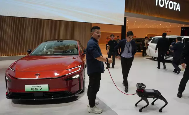 A visitor and his robotic dog stand near to the Toyota BZ7 EV model showcased at the Auto China 2026, in Beijing, Friday, April 24, 2026. (AP Photo/Andy Wong)