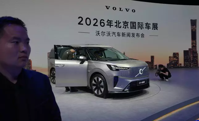 A security stands watch as visitors look at the Volvo EM90 model showcased at the Auto China 2026, in Beijing, Friday, April 24, 2026. (AP Photo/Andy Wong)
