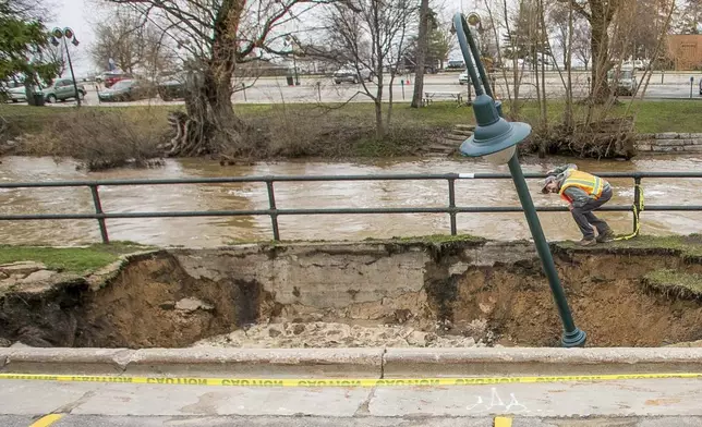 City Streets Department workers inspect a sinkhole that swallowed a street light and parts of a sidewalk along the surging Boardman/Ottaway River on Wednesday, April 15, 2026, in downtown Traverse City, Mich. (Jan-Michael Stump/Traverse City Record-Eagle via AP)