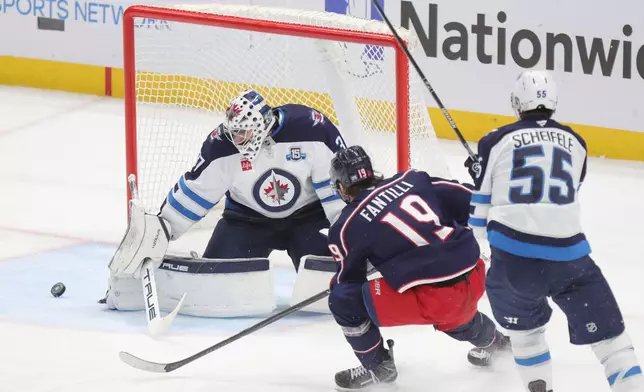 Winnipeg Jets goalie Connor Hellebuyck, left, stops a shot in front of Columbus Blue Jackets forward Adam Fantilli and Jets forward Mark Scheifele during the third period of an NHL hockey game in Columbus, Ohio, Saturday, April 4, 2026. (AP Photo/Paul Vernon)