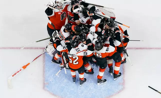 The Philadelphia Flyers gather around the net of goalie Dan Vladar, top left, as they celebrate after making the playoffs after an NHL hockey game against the Carolina Hurricanes, Monday, April 13, 2026, in Philadelphia. (AP Photo/Chris Szagola)