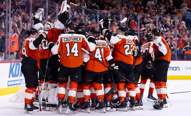 The Philadelphia Flyers gather around the net of goalie Dan Vladar, second from left, to celebrate a win and clinching a playoff berth after an NHL hockey game against the Carolina Hurricanes, Monday, April 13, 2026, in Philadelphia. (AP Photo/Chris Szagola)