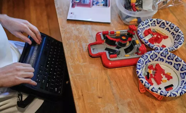 Matthew Shifrin, the founder of Bricks for the Blind, reads from a braille terminal while building a LEGO gum ball machine at his family's home, Friday, March 20, 2026, in Newton, Mass. (AP Photo/Charles Krupa)