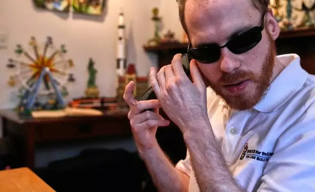 Matthew Shifrin, the founder of Bricks for the Blind, listens to directions on his phone while building a LEGO gum ball machine at his family's home, Friday, March 20, 2026, in Newton, Mass. (AP Photo/Charles Krupa)