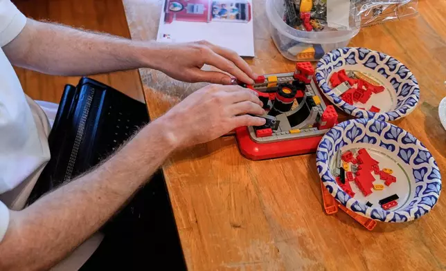 Matthew Shifrin, the founder of Bricks for the Blind, feels for specific pieces while building a LEGO gum ball machine at his family's home, Friday, March 20, 2026, in Newton, Mass. (AP Photo/Charles Krupa)