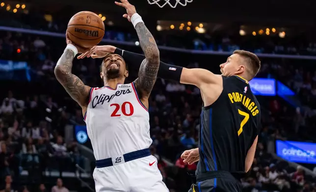 Los Angeles Clippers forward John Collins (20) shoots against Golden State Warriors center Kristaps Porzingis (7) during the first half of an NBA basketball game, Sunday, April 12, 2026, in Inglewood, Calif. (AP Photo/Ethan Swope)