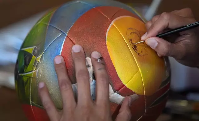 Artist Lili Cantero paints a soccer ball with images commemorating Spain's 2010 World Cup victory as part of the launch of the Wynwood United Soccer Ball Art Trail, which will showcase hand-painted soccer balls honoring historic World Cup championships inside local businesses, April 8, 2026, at Rodilla cafe in the Wynwood district of Miami. (AP Photo/Rebecca Blackwell)