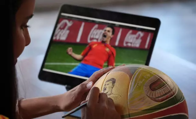Artist Lili Cantero paints a soccer ball with images commemorating Spain's 2010 World Cup victory as part of the launch of the Wynwood United Soccer Ball Art Trail, which will showcase hand-painted soccer balls honoring historic World Cup championships inside local businesses, April 8, 2026, at Rodilla cafe in the Wynwood district of Miami. (AP Photo/Rebecca Blackwell)