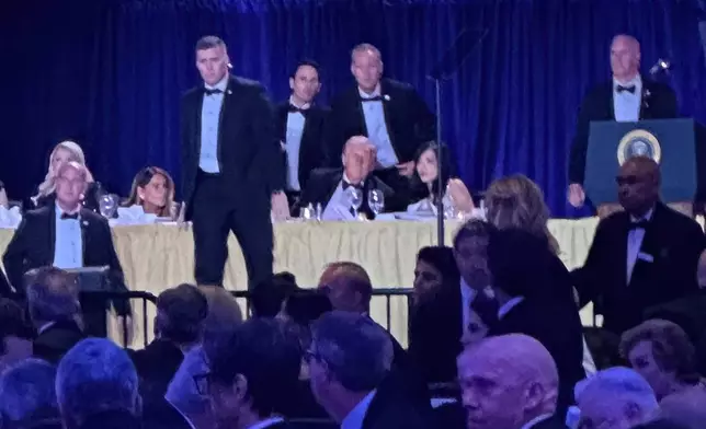U.S. Secret Service agents surround President Donald Trump before he was taken from the stage after a shooting incident outside the ballroom during the White House Correspondents Dinner, Saturday, April 25, 2026, in Washington. (AP Photo/Alex Brandon)