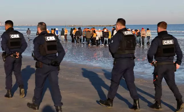 Policemen walk past migrants as they board a small boat in an attempt to reach Britain, Wednesday, April 8, 2026 in Malo-les-Bains, northern France. (AP Photo/Jean-Francois Badias)