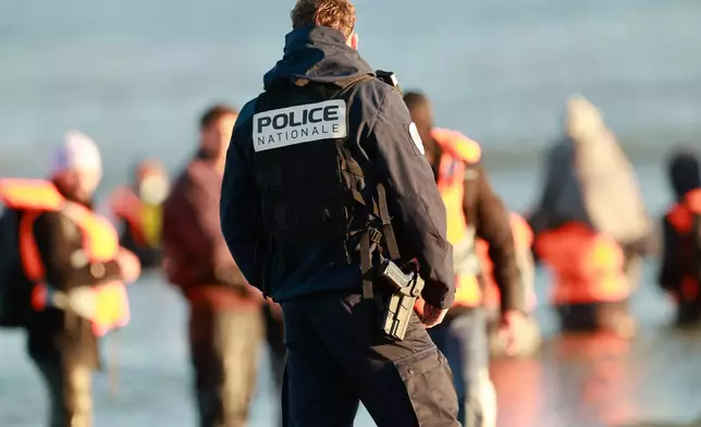 A policeman looks at migrants as they board a small boat in an attempt to reach Britain, Wednesday, April 8, 2026 in Malo-les-Bains, northern France. (AP Photo/Jean-Francois Badias)