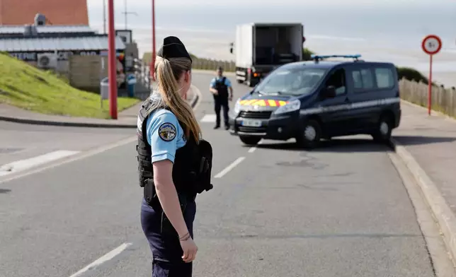 A police officer stands guard after a migrant taxi-boat accident, in Equihen-Plage, northern France. Thursday, April 9, 2026. (AP Photo/Jean-Francois Badias)