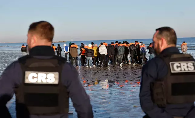Policemen look at migrants as they board a small boat in an attempt to reach Britain, Wednesday, April 8, 2026 in Malo-les-Bains, northern France. (AP Photo/Jean-Francois Badias)