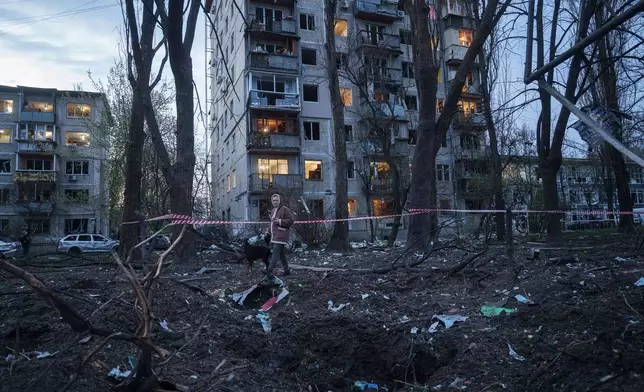 A woman with a dog walks among the rubble of a house damaged after a Russian strike on residential area in Kyiv, Ukraine, on Thursday, April 16, 2026. (AP Photo/Evgeniy Maloletka)