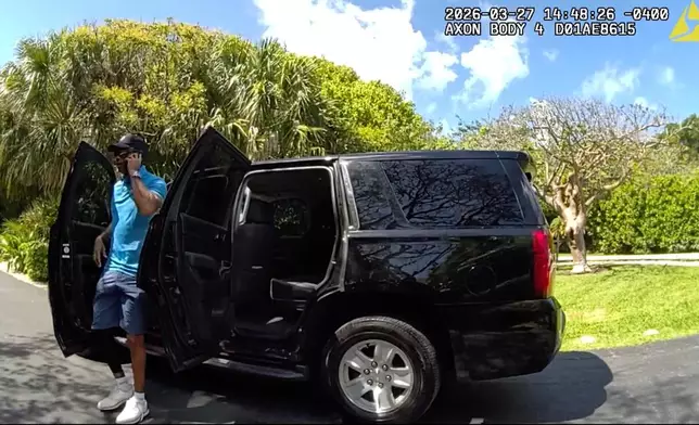 In this image from police body camera video released by the Martin County, Fla., Sheriff's Office, golfer Tiger Woods speaks on his cellphone as he steps out of an unmarked police vehicle following a car crash in Jupiter Island, Fla., Friday, March 27, 2026. (Martin County Sheriff's Office via AP)