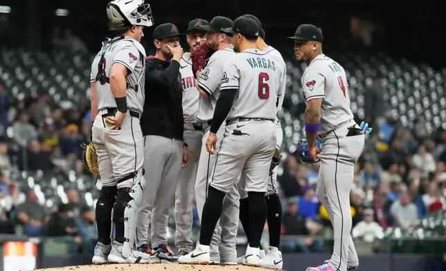 Arizona Diamondbacks pitching coach Brian Kaplan, second from left, talks to starting pitcher Merrill Kelly during the first inning of a baseball game against the Milwaukee Brewers, Tuesday, April 28, 2026, in Milwaukee. (AP Photo/Nam Y. Huh)