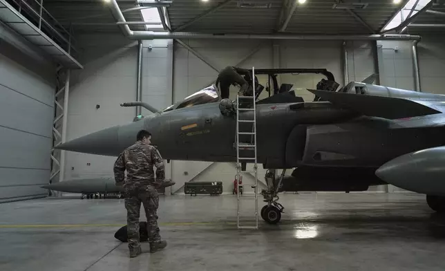 A flight-crew member climbs into the cockpit of a French air force Rafale fighter jet stationed on a NATO air-policing mission at the Siauliai Air Base in Lithuania as another member of the French detachment stands at the foot of the ladder on Sunday, April 19, 2026 (AP Photo/John Leicester)