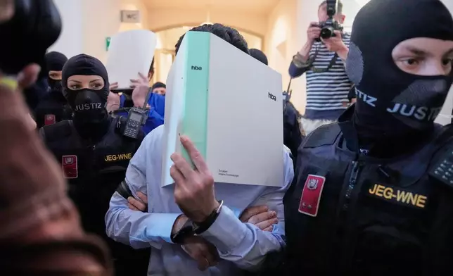 The defendants hide their faces behind file folders on their way to the courtroom in the District Court in Wiener Neustadt, Austria, where two terror suspects will stand trial Tuesday, one for plotting to carry out an attack on one of superstar singer Taylor Swift's concerts in Vienna in August 2024 and pledging allegiance to the Islamic State group, Tuesday, April 28, 2026. (AP Photo/Matthias Schrader)