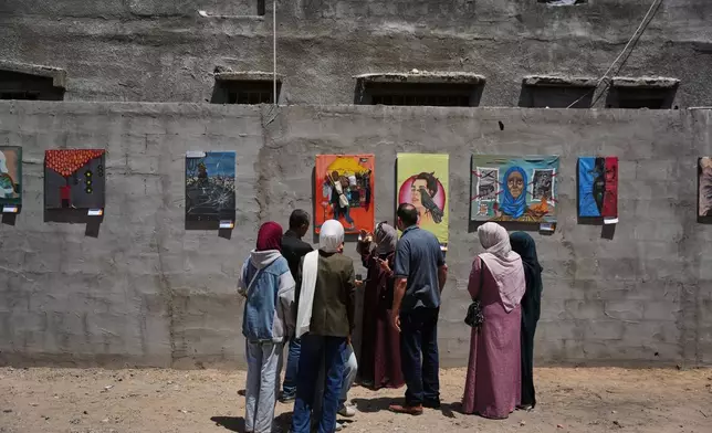 People look at paintings by Palestinian artists during an exhibition in Al-Bureij camp in the central Gaza Strip Tuesday, April 28, 2026. (AP Photo/Abdel Kareem Hana)