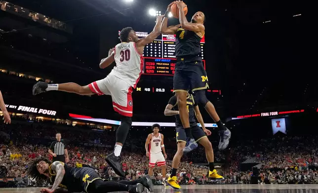 Michigan's Nimari Burnett (4) and Arizona's Tobe Awaka (30) reach for a rebound as Michigan's Elliot Cadeau, bottom, watches during the first half of an NCAA college basketball tournament semifinal game at the Final Four, Saturday, April 4, 2026, in Indianapolis. (AP Photo/Michael Conroy)