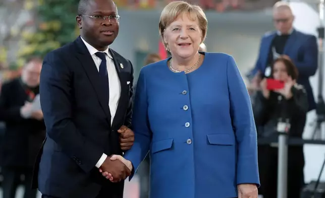 FILE - Benin's Economy and Finance Minister Romuald Wadagni, left, and German Chancellor Angela Merkel shake hands prior to a meeting at the chancellery as part of the "Compact with Africa" conference, in Berlin, Nov. 19, 2019. (AP Photo/Michael Sohn, File)