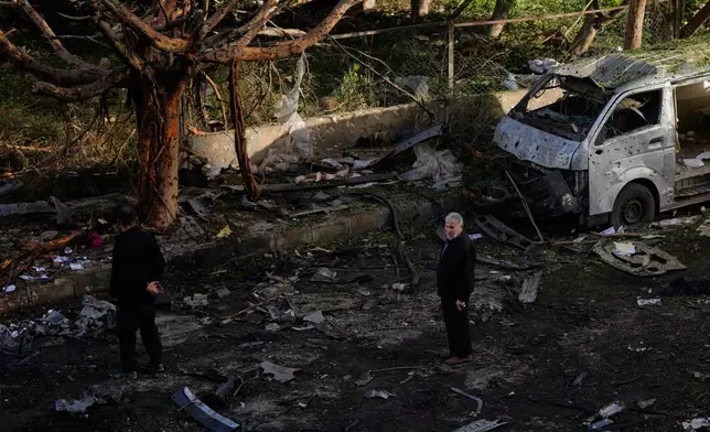 People stand near a damaged van beside scattered debris following an Israeli strike in Beirut, Lebanon, Wednesday, April 1, 2026. (AP Photo/Hassan Ammar)