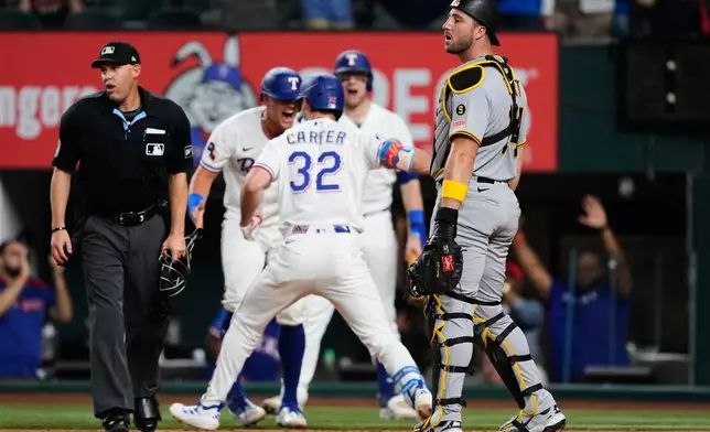 Pittsburgh Pirates catcher Joey Bart, right, and umpire Dan Merzel, left, look to the outfield as Texas Rangers' Evan Carter (32) and others celebrate Carter's inside the park home run in the third inning of a baseball game Thursday, April 23, 2026, in Arlington, Texas. (AP Photo/Tony Gutierrez)