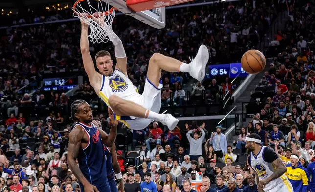 Golden State Warriors' Krystaps Porzingis (7) hangs from the rim after following a missed Stephen Curry (30) shot attemps with a dunk in the first half of an NBA play-in tournament game in Inglewood, Calif., on Wednesday, April 15, 2026. (Carlos Avila Gonzalez/San Francisco Chronicle via AP)
