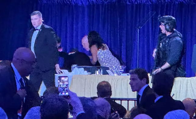 U.S. Secret Service agents surround President Donald Trump as he is taken from the stage after a shooting incident outside the ballroom during the White House Correspondents Dinner, Saturday, April 25, 2026, in Washington. (AP Photo/Mark Schiefelbein)