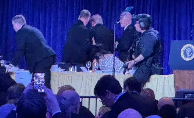 U.S. Secret Service agents surround President Donald Trump, third from left, as he is taken from the stage after a shooting incident outside the ballroom during the White House Correspondents Dinner, Saturday, April 25, 2026, in Washington. (AP Photo/Mark Schiefelbein)