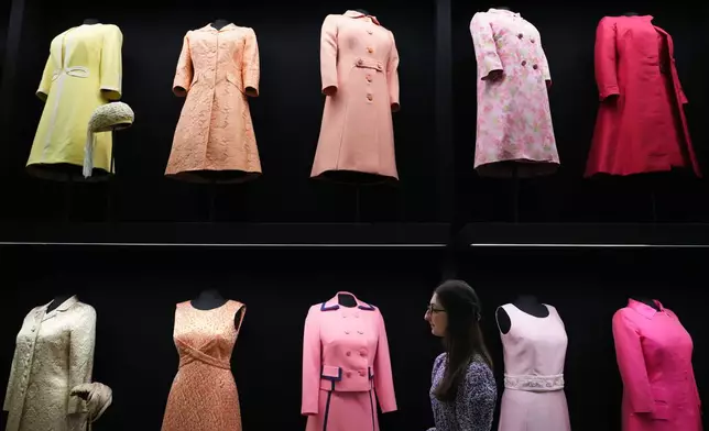 A member of Royal Collection Trust staff looks towards day wear worn by Princess Elizabeth, on display at 'Queen Elizabeth II: Her Life in Style' exhibition, to mark the centenary of the late queen's birth, at The King's Gallery at Buckingham Palace in London, Thursday, April 9, 2026. (AP Photo/Kirsty Wigglesworth)