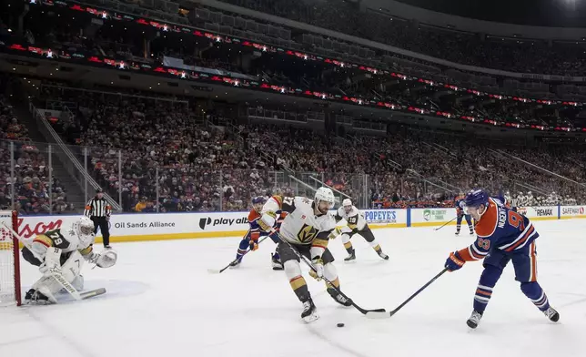 Vegas Golden Knights' Shea Theodore (27) and Edmonton Oilers' Ryan Nugent-Hopkins (93) battle for the puck as Golden Knight's goalie Carter Hart (79) defends during the second period of an NHL hockey game in Edmonton, Alberta, on Saturday April 4, 2026. (Jason Franson/The Canadian Press via AP)