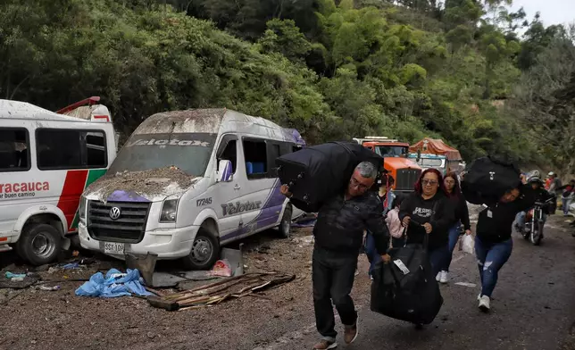 Travelers walk past vehicles damaged in an attack on the Pan-American Highway in Cajibio, Colombia, Sunday, April 26, 2026, where at least a dozen people were killed in an attack authorities blamed on dissident groups of the former FARC rebels. (AP Photo/Santiago Saldarriaga)
