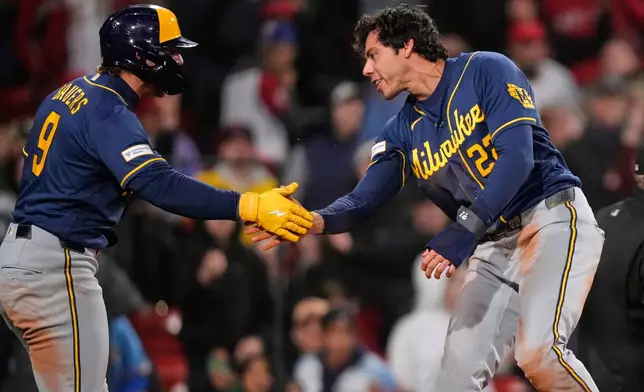 Milwaukee Brewers' Christian Yelich, right, is congratulated by Jake Bauers (9) after scoring on a single by Garrett Mitchell during the eighth inning of a baseball game against the Boston Red Sox at Fenway Park, Monday, April 6, 2026, in Boston. (AP Photo/Charles Krupa)