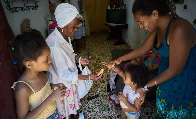 Yuneisy Riviaux helps her daughter Seinet to reach for a banana from a friend at their home in Havana, Cuba, Wednesday, March 25, 2026. (AP Photo/Ramon Espinosa)