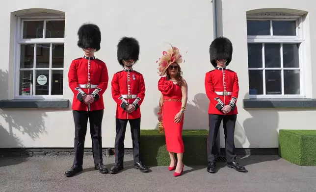 A racegoer poses for a picture with soldiers on Ladies Day, the second day of the Grand National Horse Racing festival, at Aintree racecourse, near Liverpool, England, Friday, April 10, 2026. (AP Photo/Jon Super)