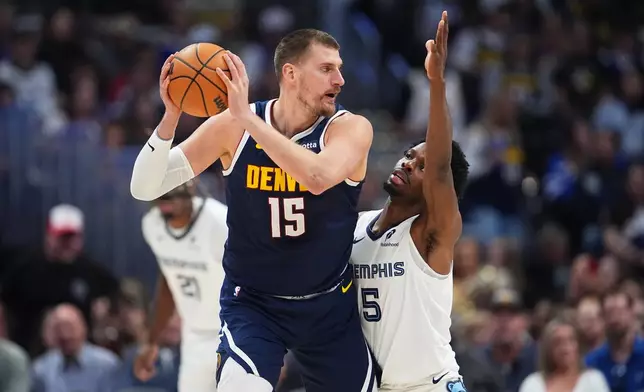 Denver Nuggets center Nikola Jokić, left, looks to pass the ball as Memphis Grizzlies forward Toby Okani defends in the first half of an NBA basketball game Wednesday, April 8, 2026, in Denver. (AP Photo/David Zalubowski)