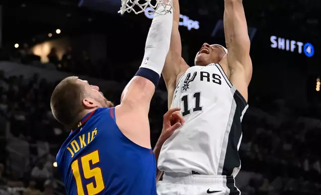 San Antonio Spurs forward Carter Bryant (11) dunks against Denver Nuggets center Nikola Jokic during the first half of an NBA basketball game, Sunday, April 12, 2026, in San Antonio. (AP Photo/Darren Abate)