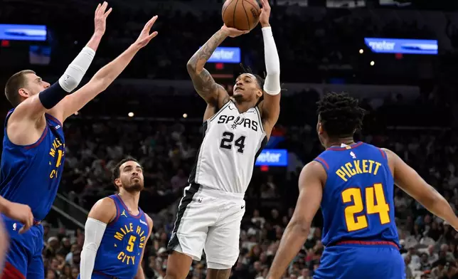 San Antonio Spurs guard Devin Vassell shoots against Denver Nuggets' Nikola Jokic, left, Tyus Jones (5) and Jalen Pickett, right, during the first half of an NBA basketball game, Sunday, April 12, 2026, in San Antonio. (AP Photo/Darren Abate)